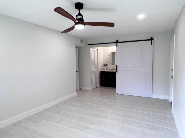 unfurnished bedroom with ceiling fan, a barn door, and light hardwood / wood-style floors