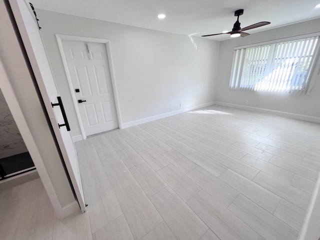 unfurnished room featuring ceiling fan, a barn door, and light wood-type flooring