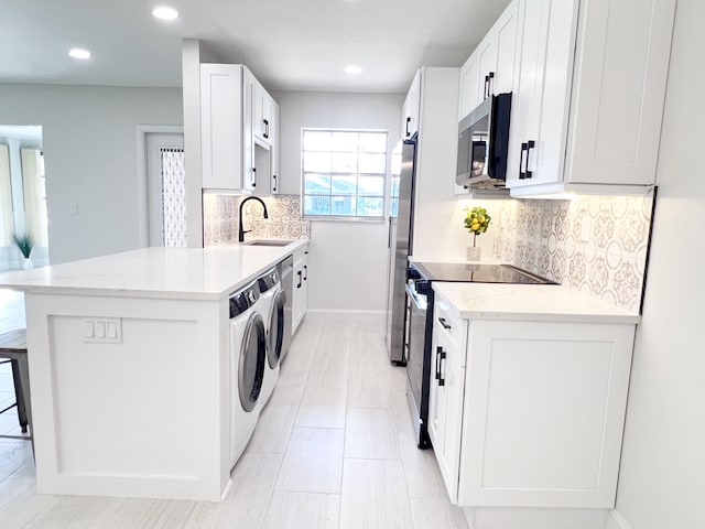 kitchen with sink, appliances with stainless steel finishes, white cabinetry, light stone counters, and washing machine and clothes dryer