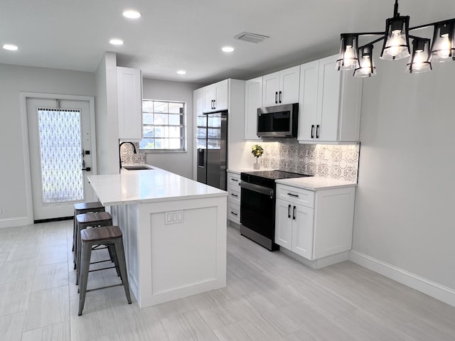 kitchen with sink, appliances with stainless steel finishes, hanging light fixtures, white cabinets, and a kitchen island