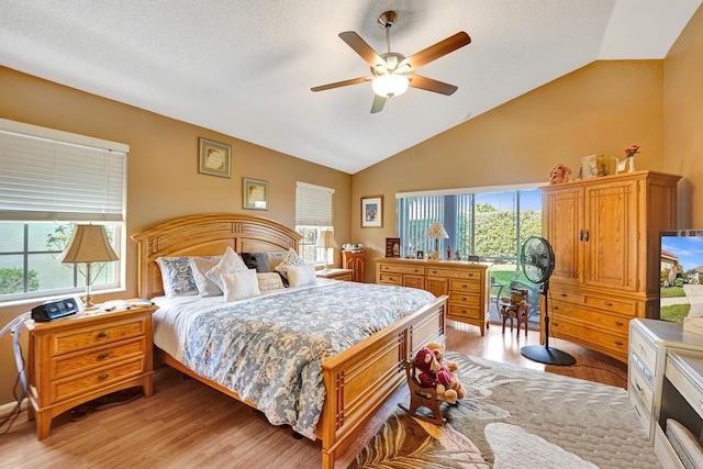 bedroom with ceiling fan, vaulted ceiling, a textured ceiling, and light wood-type flooring