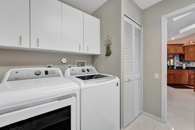 clothes washing area with cabinets, washer and dryer, and light tile patterned floors