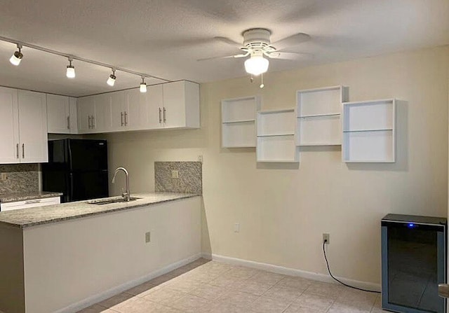 kitchen with sink, white cabinetry, light stone counters, black refrigerator, and ceiling fan