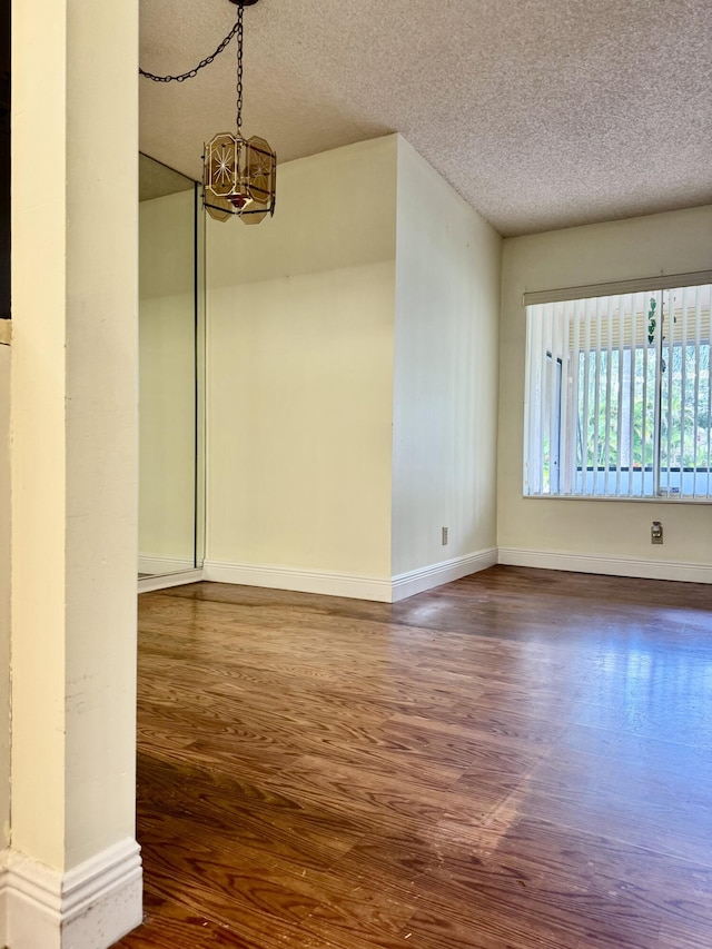 spare room featuring dark hardwood / wood-style flooring, a textured ceiling, and a notable chandelier