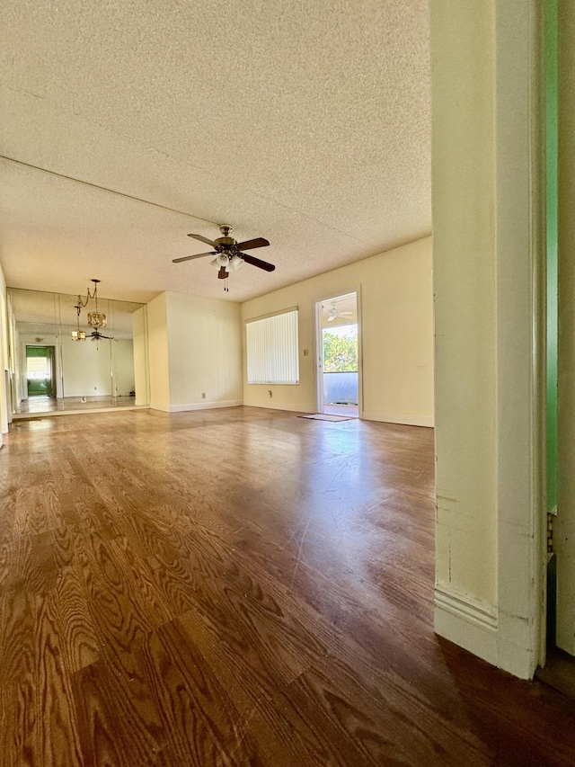 empty room with ceiling fan with notable chandelier, a textured ceiling, and dark hardwood / wood-style flooring