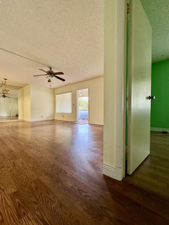 empty room with dark hardwood / wood-style floors, ceiling fan with notable chandelier, and a textured ceiling