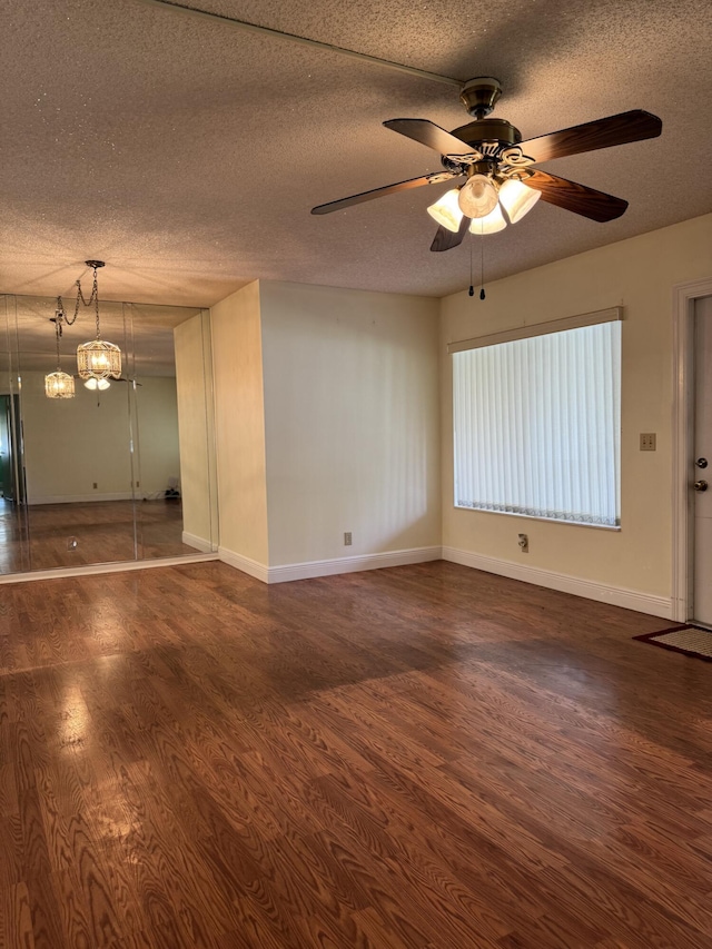 spare room with dark wood-type flooring, ceiling fan with notable chandelier, and a textured ceiling