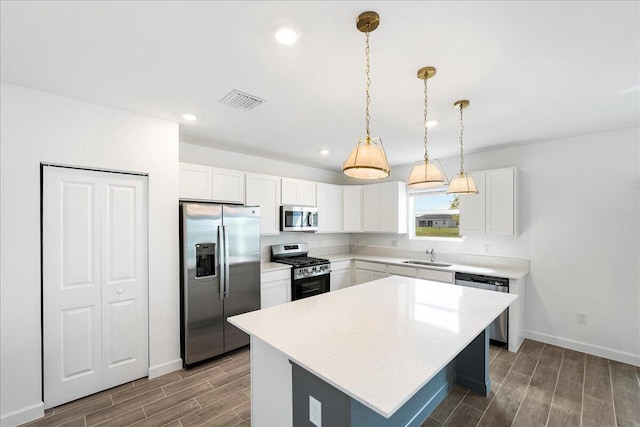 kitchen featuring appliances with stainless steel finishes, decorative light fixtures, white cabinetry, sink, and a center island