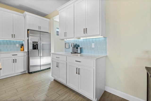 kitchen with backsplash, white cabinets, light hardwood / wood-style floors, and stainless steel fridge with ice dispenser