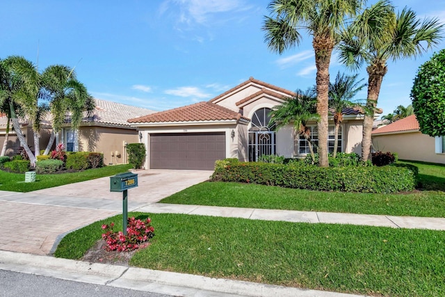 mediterranean / spanish-style home with a garage, stucco siding, a tile roof, decorative driveway, and a front yard