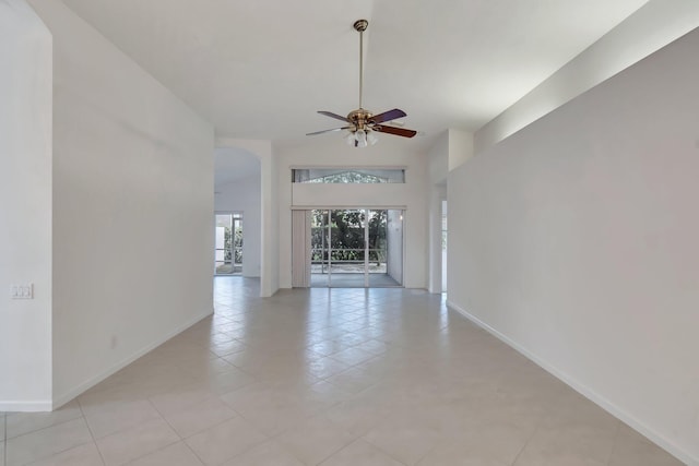 unfurnished living room with baseboards, arched walkways, a ceiling fan, and light tile patterned flooring