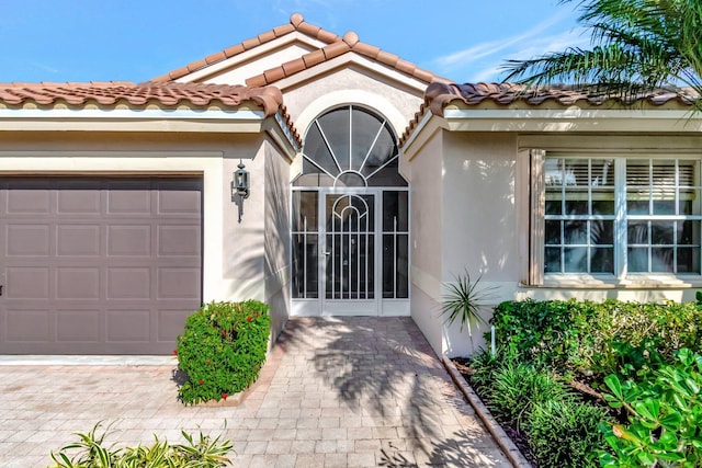 view of exterior entry featuring an attached garage, a tile roof, and stucco siding