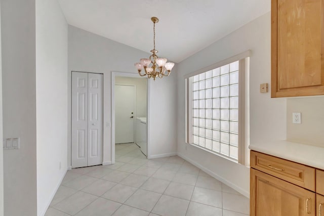 unfurnished dining area featuring washer / dryer, light tile patterned floors, baseboards, lofted ceiling, and a chandelier