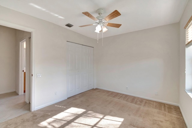 unfurnished bedroom with a closet, visible vents, light carpet, ceiling fan, and baseboards