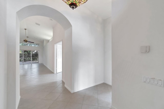 corridor with arched walkways, light tile patterned floors, lofted ceiling, and baseboards