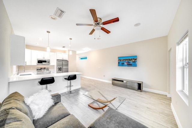 living room with ceiling fan, plenty of natural light, sink, and light wood-type flooring