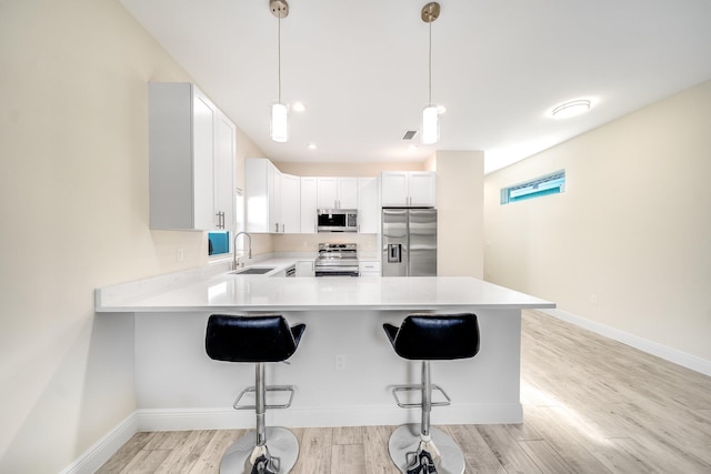 kitchen with pendant lighting, sink, white cabinetry, stainless steel appliances, and a kitchen breakfast bar