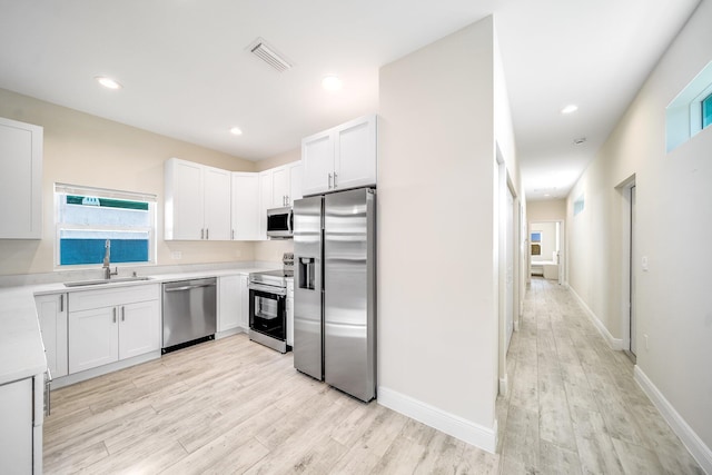 kitchen with stainless steel appliances, sink, white cabinets, and light hardwood / wood-style floors