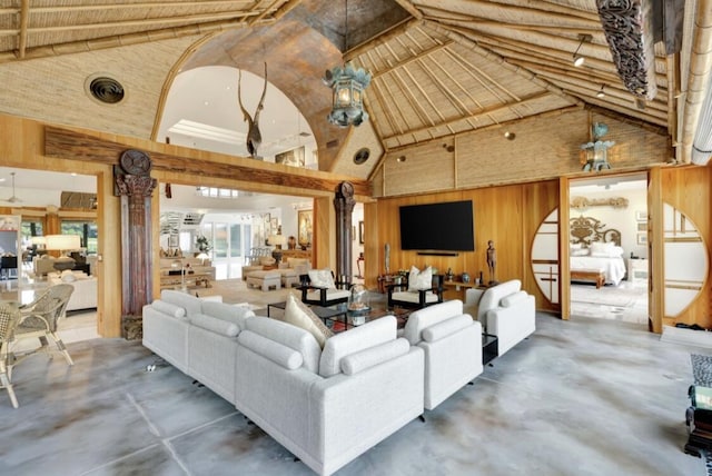 living room with high vaulted ceiling, concrete floors, decorative columns, and wood walls