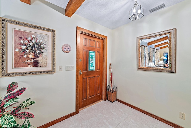 foyer with beam ceiling, light tile patterned flooring, a notable chandelier, and a textured ceiling