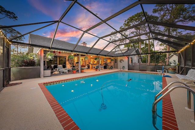 pool at dusk featuring glass enclosure and a patio area