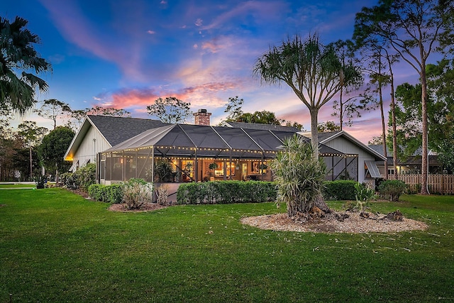 back house at dusk featuring a lanai and a lawn