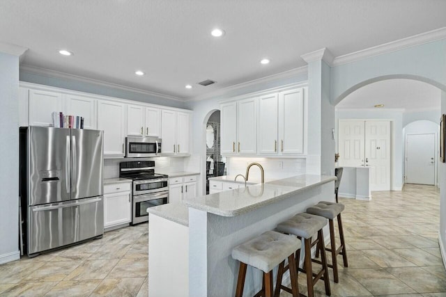 kitchen featuring visible vents, a kitchen breakfast bar, white cabinetry, arched walkways, and appliances with stainless steel finishes