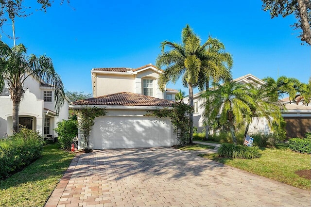 mediterranean / spanish house with decorative driveway, an attached garage, stucco siding, and a tiled roof