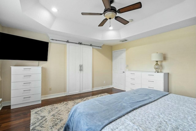 bedroom featuring dark wood-type flooring, a raised ceiling, ceiling fan, and a barn door