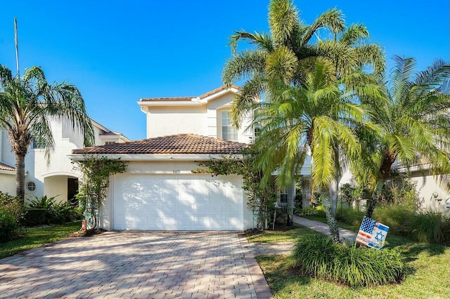 mediterranean / spanish house featuring a tiled roof, stucco siding, an attached garage, and decorative driveway