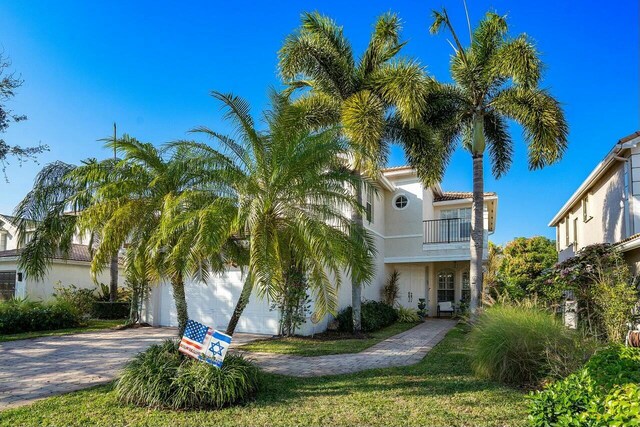 view of front of home featuring a tiled roof, stucco siding, decorative driveway, a garage, and a balcony