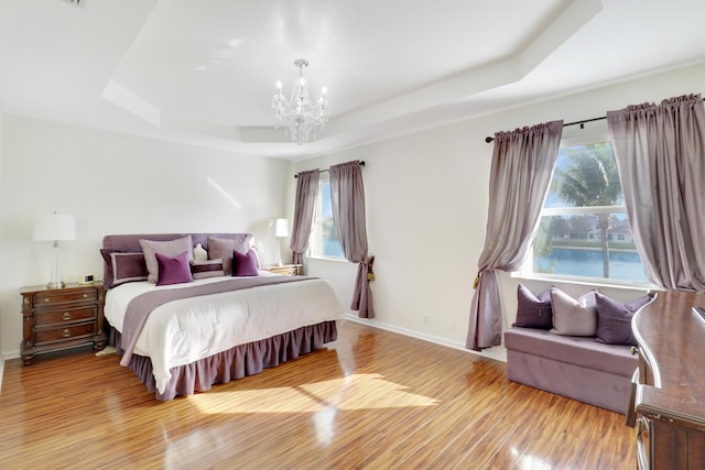 bedroom featuring multiple windows, a tray ceiling, and light wood-type flooring