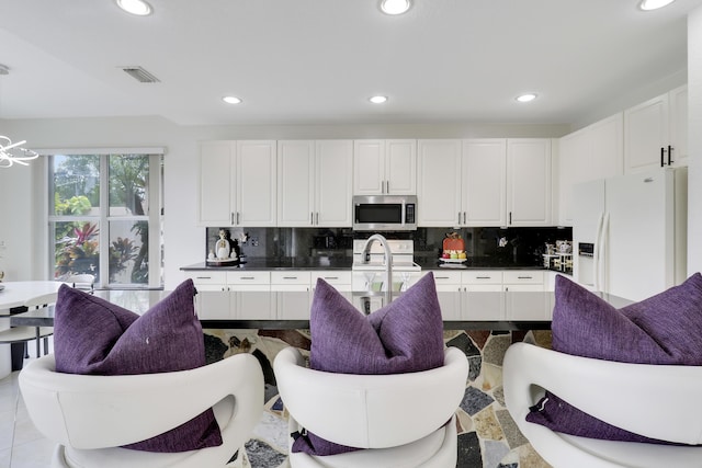 kitchen with white cabinetry, backsplash, white fridge with ice dispenser, and stove