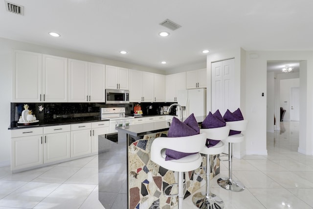 kitchen with light tile patterned flooring, white appliances, a kitchen breakfast bar, and white cabinets