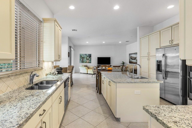 kitchen featuring sink, stainless steel appliances, cream cabinets, light stone countertops, and a kitchen island