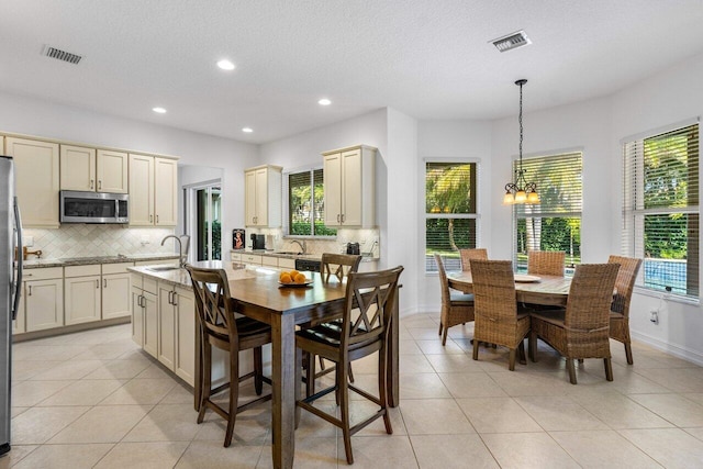 kitchen featuring light tile patterned flooring, decorative backsplash, hanging light fixtures, black appliances, and cream cabinets