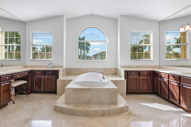 bathroom featuring vaulted ceiling, a healthy amount of sunlight, a relaxing tiled tub, and vanity