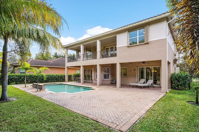 back of house featuring ceiling fan, a balcony, a patio, and a lawn