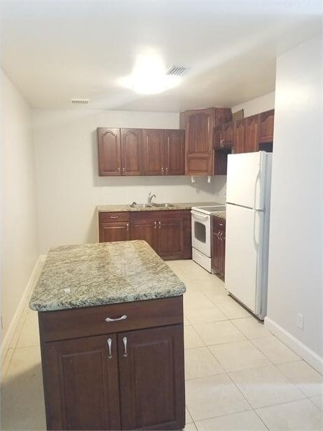 kitchen featuring sink, light stone counters, a center island, light tile patterned floors, and white appliances