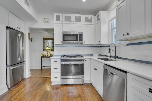 kitchen featuring appliances with stainless steel finishes, tasteful backsplash, sink, white cabinets, and hardwood / wood-style flooring