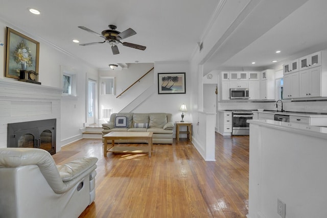 living room featuring sink, ceiling fan, crown molding, a brick fireplace, and light wood-type flooring