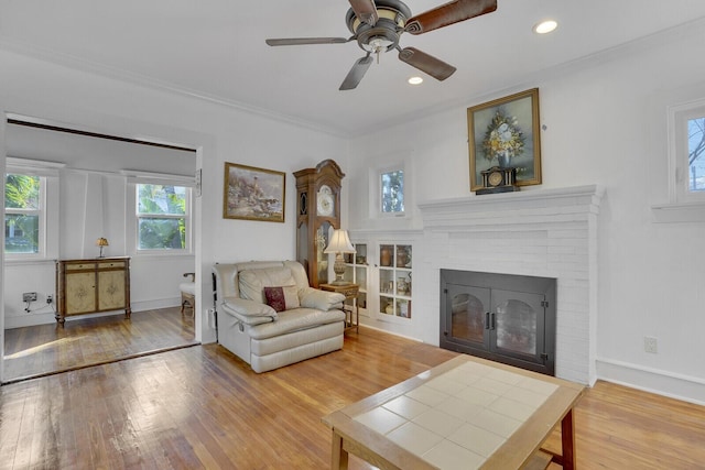 living room with a fireplace, wood-type flooring, ornamental molding, and ceiling fan