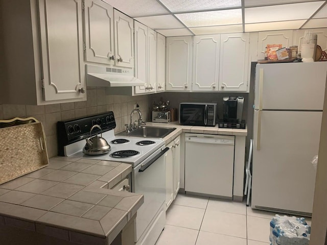 kitchen featuring light tile patterned flooring, sink, white cabinets, tile counters, and white appliances