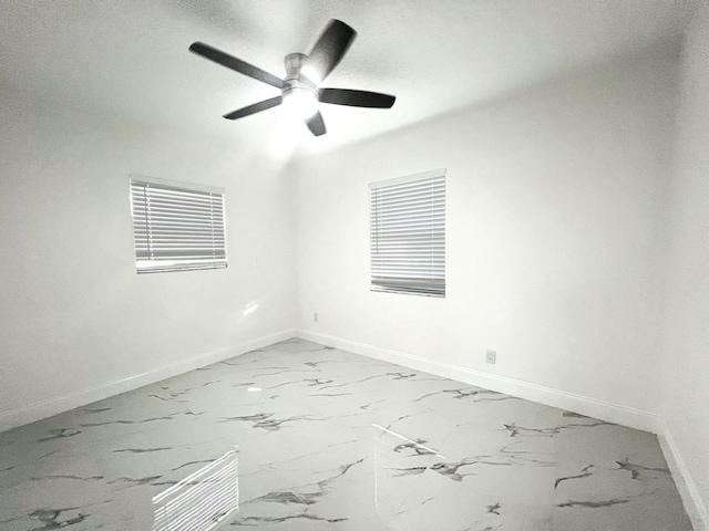 spare room with marble finish floor, a ceiling fan, and baseboards