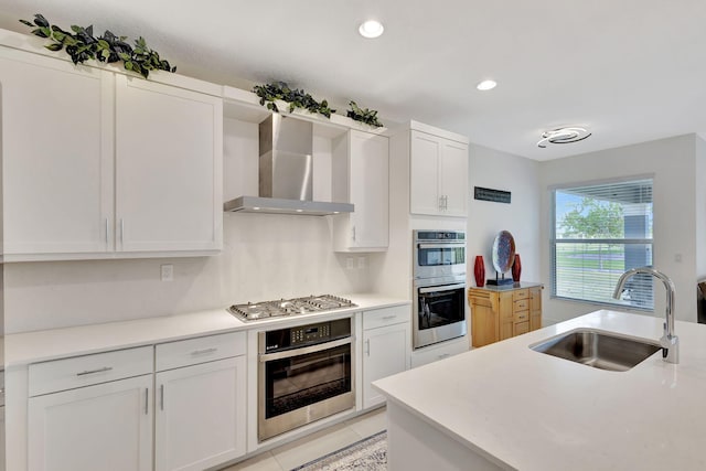 kitchen with sink, white cabinetry, light tile patterned floors, stainless steel appliances, and wall chimney range hood