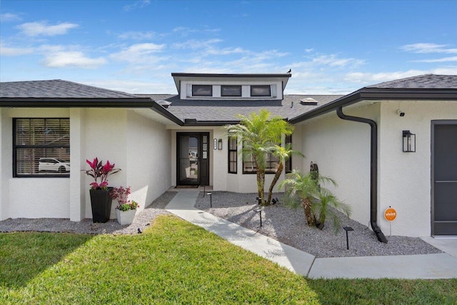 view of exterior entry with a shingled roof, a lawn, and stucco siding