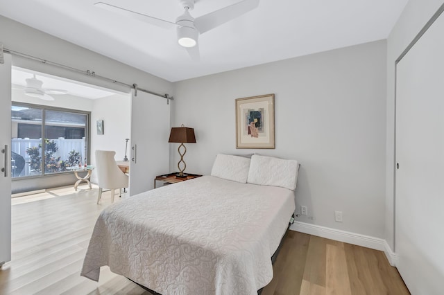 bedroom with hardwood / wood-style flooring, a barn door, and ceiling fan