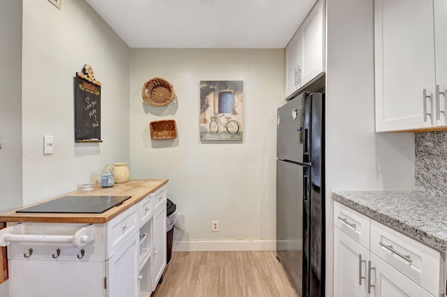 kitchen featuring white cabinetry, decorative backsplash, light wood-type flooring, and black fridge