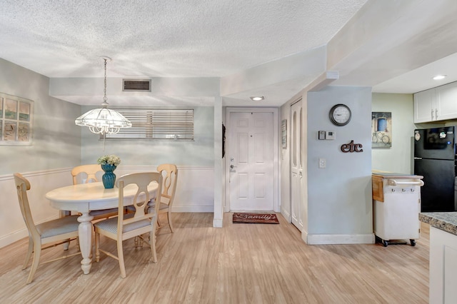 dining area with a chandelier, a textured ceiling, and light wood-type flooring