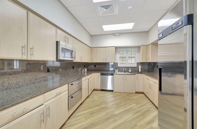 kitchen with stainless steel appliances, sink, dark stone countertops, and light hardwood / wood-style flooring